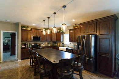 Country l-shaped vinyl floor and brown floor kitchen photo in Other with a farmhouse sink, beaded inset cabinets, brown cabinets, granite countertops, black backsplash, stainless steel appliances, an island and black countertops