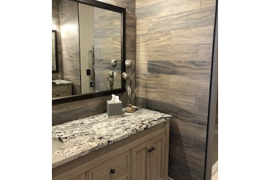 Mid-sized master brown tile and wood-look tile porcelain tile, gray floor, single-sink and wood wall alcove shower photo in Indianapolis with distressed cabinets, brown walls, an undermount sink, granite countertops, a hinged shower door, multicolored countertops, a niche and a freestanding vanity