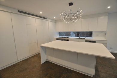 Design ideas for a large contemporary galley open plan kitchen in Sydney with a double-bowl sink, white cabinets, glass sheet splashback, stainless steel appliances, concrete floors, with island and grey floor.