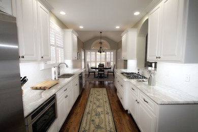 Example of a classic galley brown floor open concept kitchen design in Other with white cabinets, stainless steel appliances, no island and gray countertops