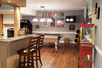 Example of a large classic walk-out laminate floor and brown floor basement game room design in Richmond with gray walls, a standard fireplace and a brick fireplace