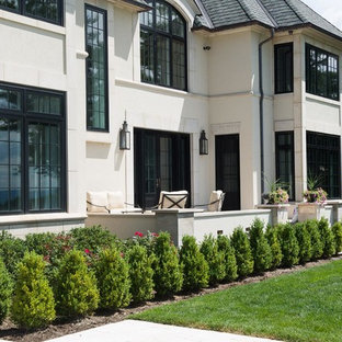 Новый формат декора квартиры: огромный, трехэтажный фасад частного дома бежевого цвета в стиле современная классика с облицовкой из цементной штукатурки, полувальмовой крышей и зеленой крышей