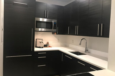 This is an example of a small contemporary u-shaped separate kitchen in New York with an undermount sink, flat-panel cabinets, black cabinets, quartz benchtops, white splashback, panelled appliances, laminate floors, no island, beige floor and white benchtop.