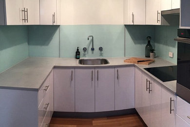Esempio di una piccola cucina ad U moderna chiusa con lavello a vasca singola, ante bianche, top in cemento, elettrodomestici neri e nessuna isola