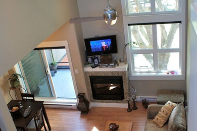 Large trendy loft-style light wood floor living room photo in Vancouver with beige walls, a corner fireplace, a stone fireplace and a wall-mounted tv