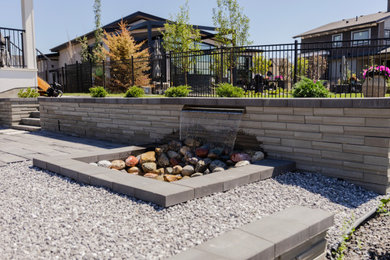 Design ideas for a large modern backyard concrete paver waterfall in Calgary.