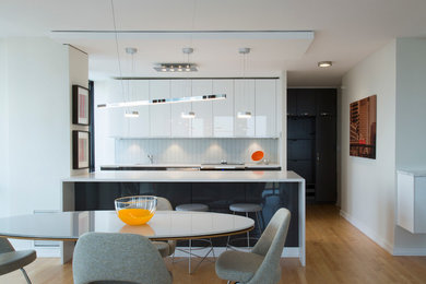 Mid-sized trendy galley light wood floor eat-in kitchen photo in Chicago with a single-bowl sink, flat-panel cabinets, white cabinets, quartz countertops, white backsplash, glass sheet backsplash, stainless steel appliances and an island