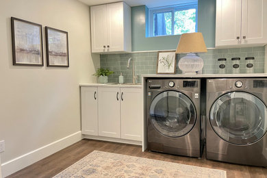 Mid-sized transitional vinyl floor and brown floor dedicated laundry room photo in Montreal with a drop-in sink, shaker cabinets, white cabinets, laminate countertops, green backsplash, porcelain backsplash, beige walls, a side-by-side washer/dryer and white countertops
