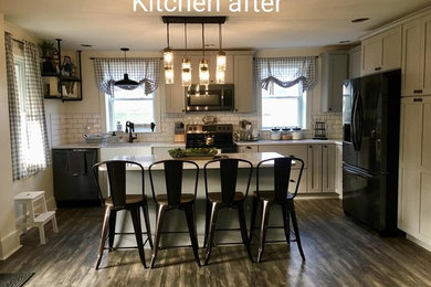 Example of a mid-sized transitional l-shaped dark wood floor and multicolored floor eat-in kitchen design in Other with a farmhouse sink, shaker cabinets, gray cabinets, quartz countertops, white backsplash, subway tile backsplash, black appliances, an island and white countertops