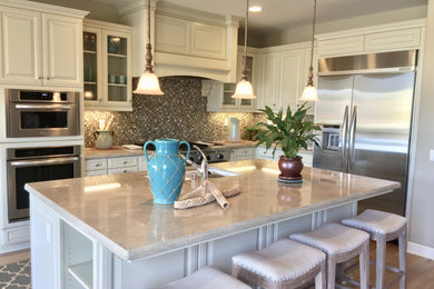 Large beach style l-shaped light wood floor eat-in kitchen photo in Orange County with a double-bowl sink, recessed-panel cabinets, white cabinets, limestone countertops, multicolored backsplash, mosaic tile backsplash, stainless steel appliances, an island and beige countertops