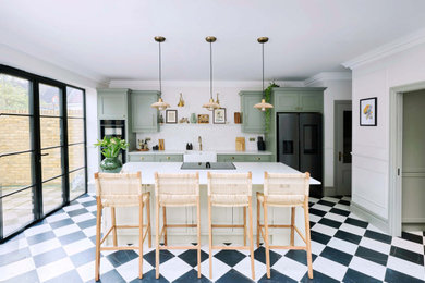 Photo of a large victorian single-wall open plan kitchen in London with a single-bowl sink, shaker cabinets, green cabinets, quartz worktops, white splashback, black appliances, an island, multi-coloured floors and white worktops.