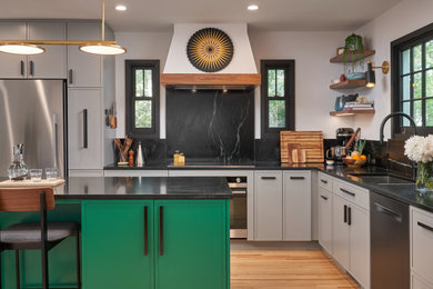 Kitchen - mid-sized transitional l-shaped light wood floor kitchen idea in Minneapolis with an undermount sink, shaker cabinets, gray cabinets, soapstone countertops, black backsplash, stone slab backsplash, stainless steel appliances, an island and black countertops