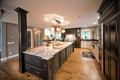 This is an example of a mid-sized transitional l-shaped kitchen in Grand Rapids with a farmhouse sink, raised-panel cabinets, black cabinets, marble benchtops, stainless steel appliances, medium hardwood floors and with island.