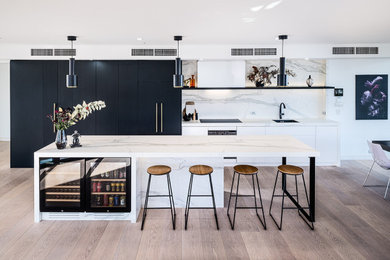 Large modern galley open plan kitchen in Melbourne with an undermount sink, flat-panel cabinets, white cabinets, quartz benchtops, white splashback, engineered quartz splashback, black appliances, laminate floors, brown floor and white benchtop.