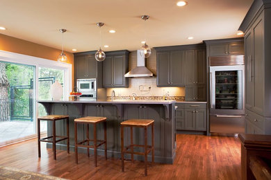 Mid-sized transitional l-shaped medium tone wood floor and brown floor open concept kitchen photo in Atlanta with an undermount sink, recessed-panel cabinets, gray cabinets, granite countertops, white backsplash, glass tile backsplash, stainless steel appliances and an island
