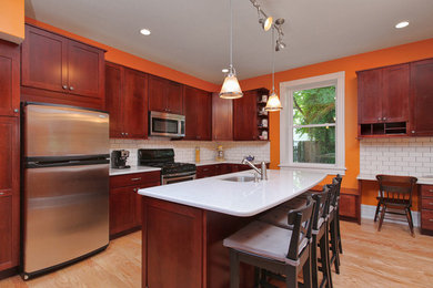 Example of a large classic l-shaped light wood floor eat-in kitchen design in Philadelphia with an undermount sink, recessed-panel cabinets, dark wood cabinets, quartzite countertops, white backsplash, ceramic backsplash, stainless steel appliances and an island