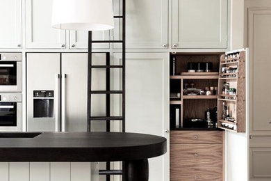 Photo of a large single-wall open plan kitchen in London with an integrated sink, shaker cabinets, green cabinets, granite worktops, black splashback, stone slab splashback, stainless steel appliances, medium hardwood flooring, an island, brown floors and black worktops.