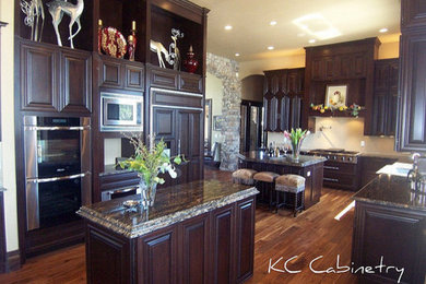 Large elegant u-shaped medium tone wood floor enclosed kitchen photo in Denver with a drop-in sink, raised-panel cabinets, dark wood cabinets, beige backsplash, stainless steel appliances and two islands