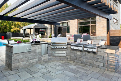 Photo of a mid-sized traditional backyard patio in New York with an outdoor kitchen, concrete pavers and a pergola.