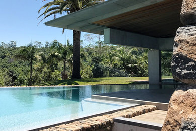 Photo of a large side yard l-shaped infinity pool in Gold Coast - Tweed with natural stone pavers.