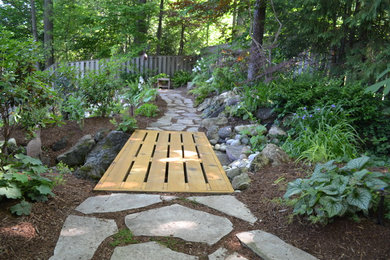 Photo of a traditional sloped partial sun garden for summer in Toronto with a retaining wall and natural stone pavers.