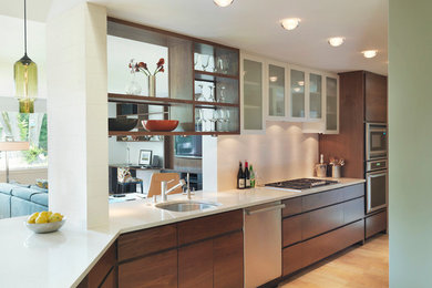Example of a minimalist u-shaped light wood floor kitchen design in Boston with an undermount sink, dark wood cabinets, solid surface countertops, white backsplash, subway tile backsplash, stainless steel appliances and flat-panel cabinets