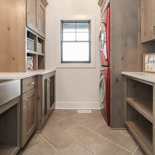 Imagen de cuarto de lavado campestre, de tamaño medio, con fregadero sobremueble, armarios estilo shaker, puertas de armario con efecto envejecido, encimera de cuarzo compacto, paredes blancas, suelo de baldosas de cerámica, lavadora y secadora apiladas, suelo gris y encimeras blancas