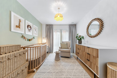 Photo of a medium sized contemporary gender neutral nursery in London with green walls, plywood flooring, brown floors and a feature wall.
