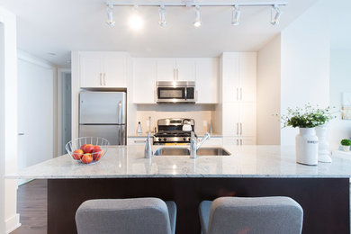Example of a small trendy galley medium tone wood floor eat-in kitchen design in Toronto with an undermount sink, shaker cabinets, white cabinets, granite countertops, beige backsplash, stone tile backsplash, stainless steel appliances and an island