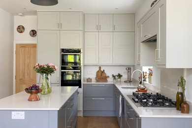 Mid-sized elegant medium tone wood floor kitchen photo in London with shaker cabinets, gray cabinets, quartzite countertops, white backsplash, quartz backsplash, an island and white countertops