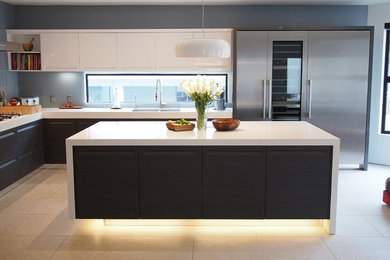 Large modern l-shaped eat-in kitchen in Los Angeles with an undermount sink, flat-panel cabinets, dark wood cabinets, grey splashback, glass sheet splashback, stainless steel appliances, porcelain floors, with island, quartz benchtops, beige floor and white benchtop.