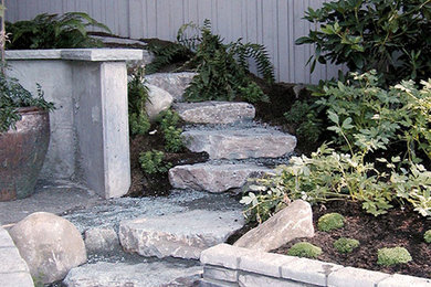 This is an example of an expansive contemporary backyard partial sun garden for summer in Seattle with a retaining wall and natural stone pavers.