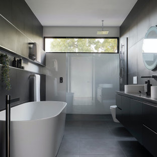 Mid-sized modern master bathroom in Sydney with recessed-panel cabinets, grey cabinets, a freestanding tub, an open shower, a wall-mount toilet, gray tile, ceramic tile, grey walls, ceramic floors, a trough sink, engineered quartz benchtops, grey floor, an open shower, grey benchtops, a niche, a double vanity, a floating vanity, recessed and panelled walls.