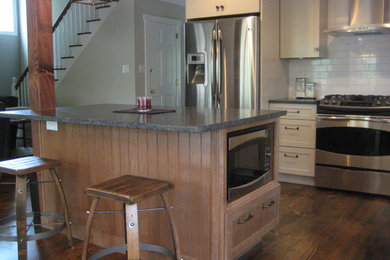 Example of a mid-sized mountain style l-shaped dark wood floor open concept kitchen design in Philadelphia with shaker cabinets, white cabinets, granite countertops, white backsplash, subway tile backsplash, stainless steel appliances, an island and a farmhouse sink