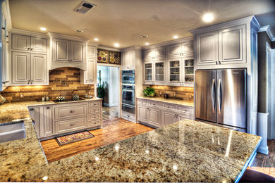 Inspiration for a mid-sized timeless u-shaped medium tone wood floor and brown floor eat-in kitchen remodel in Other with a double-bowl sink, raised-panel cabinets, white cabinets, granite countertops, beige backsplash, stainless steel appliances, a peninsula and stone tile backsplash