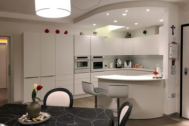 Immagine di una cucina contemporanea di medie dimensioni con lavello a doppia vasca, ante lisce, ante bianche, top in superficie solida, paraspruzzi bianco, paraspruzzi in gres porcellanato, elettrodomestici da incasso, pavimento in gres porcellanato, penisola, pavimento marrone e top bianco