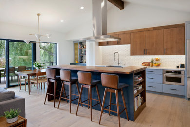 Inspiration for a mid-sized mid-century modern galley medium tone wood floor open concept kitchen remodel in Seattle with an undermount sink, flat-panel cabinets, medium tone wood cabinets, quartz countertops, white backsplash, mosaic tile backsplash, stainless steel appliances, an island and white countertops