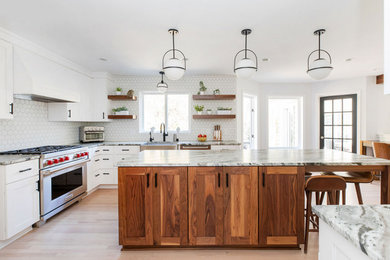 Example of a large transitional l-shaped light wood floor, beige floor and exposed beam open concept kitchen design in Other with a farmhouse sink, shaker cabinets, white cabinets, marble countertops, white backsplash, mosaic tile backsplash, stainless steel appliances, an island and multicolored countertops