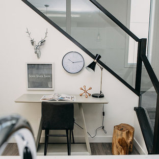 Design ideas for a small modern study in Edmonton with white walls, medium hardwood flooring, a standard fireplace, a plastered fireplace surround, a freestanding desk and brown floors.