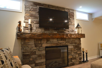 Mid-sized elegant underground laminate floor and brown floor basement photo in Toronto with a standard fireplace, a stone fireplace and beige walls