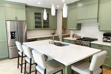 Example of a mid-sized transitional l-shaped light wood floor eat-in kitchen design in Toronto with an undermount sink, recessed-panel cabinets, green cabinets, quartz countertops, white backsplash, porcelain backsplash, stainless steel appliances, an island and white countertops