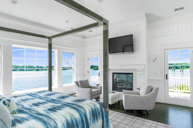 Beach style bedroom in Baltimore with white walls, dark hardwood floors, a standard fireplace, brown floor and planked wall panelling.