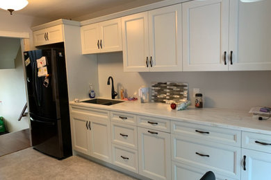 Diseño de cocina tradicional renovada de tamaño medio cerrada sin isla con fregadero encastrado, armarios con paneles empotrados, puertas de armario grises, encimera de acrílico, electrodomésticos negros y encimeras blancas