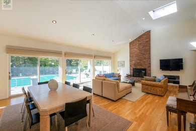 Example of a large open concept light wood floor, beige floor and vaulted ceiling living room design in New York with white walls, a standard fireplace, a brick fireplace and a wall-mounted tv