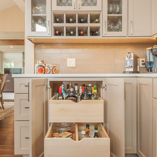 Ejemplo de cocina en L, clásica renovada, abierta, con armarios tipo vitrina, puertas de armario beige, salpicadero beige, salpicadero de azulejos tipo metro, fregadero bajoencimera, encimera de cuarcita, electrodomésticos de acero inoxidable, suelo de madera en tonos medios, una isla y suelo marrón