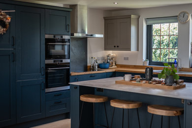 Design ideas for a medium sized rustic u-shaped open plan kitchen in Other with a built-in sink, shaker cabinets, wood worktops, black splashback, slate splashback, stainless steel appliances and an island.