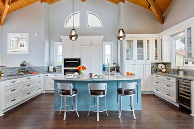 Example of a huge beach style u-shaped dark wood floor open concept kitchen design in Tampa with a farmhouse sink, shaker cabinets, soapstone countertops, multicolored backsplash, glass tile backsplash, stainless steel appliances, an island and white cabinets