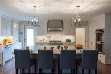 This is an example of a traditional u-shaped eat-in kitchen in Philadelphia with a farmhouse sink, recessed-panel cabinets, white cabinets, granite benchtops, white splashback, ceramic splashback, stainless steel appliances, dark hardwood floors, with island, brown floor and grey benchtop.