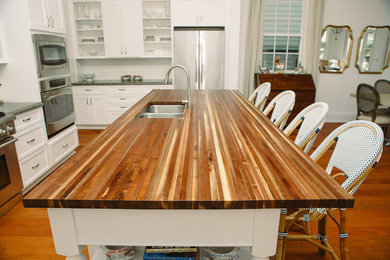Example of a large trendy medium tone wood floor and brown floor eat-in kitchen design in New Orleans with a double-bowl sink, recessed-panel cabinets, white cabinets, wood countertops, stainless steel appliances, an island and brown countertops