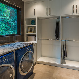 Idéer för funkis tvättstugor enbart för tvätt, med släta luckor, vita skåp, granitbänkskiva, klinkergolv i porslin och en tvättmaskin och torktumlare bredvid varandra